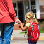 A photo of a father walking little daughter with backpack to school or daycare