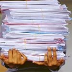 A photo of a person carrying a pile of documents
