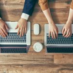 A stock photo of male and female typing on different laptops