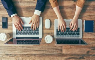 A stock photo of male and female typing on different laptops