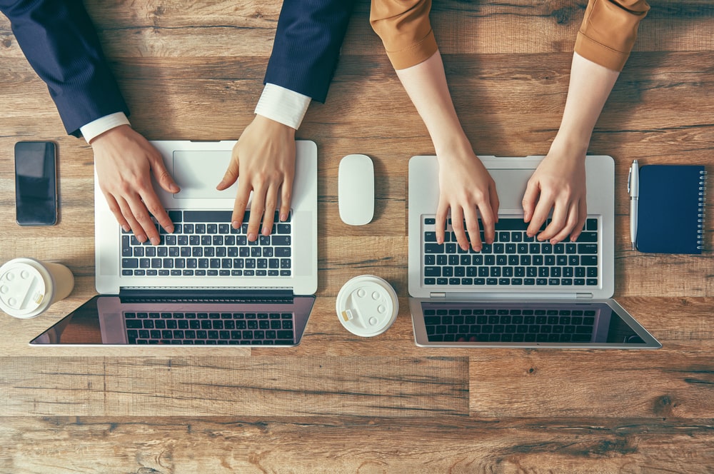 A stock photo of male and female typing on different laptops