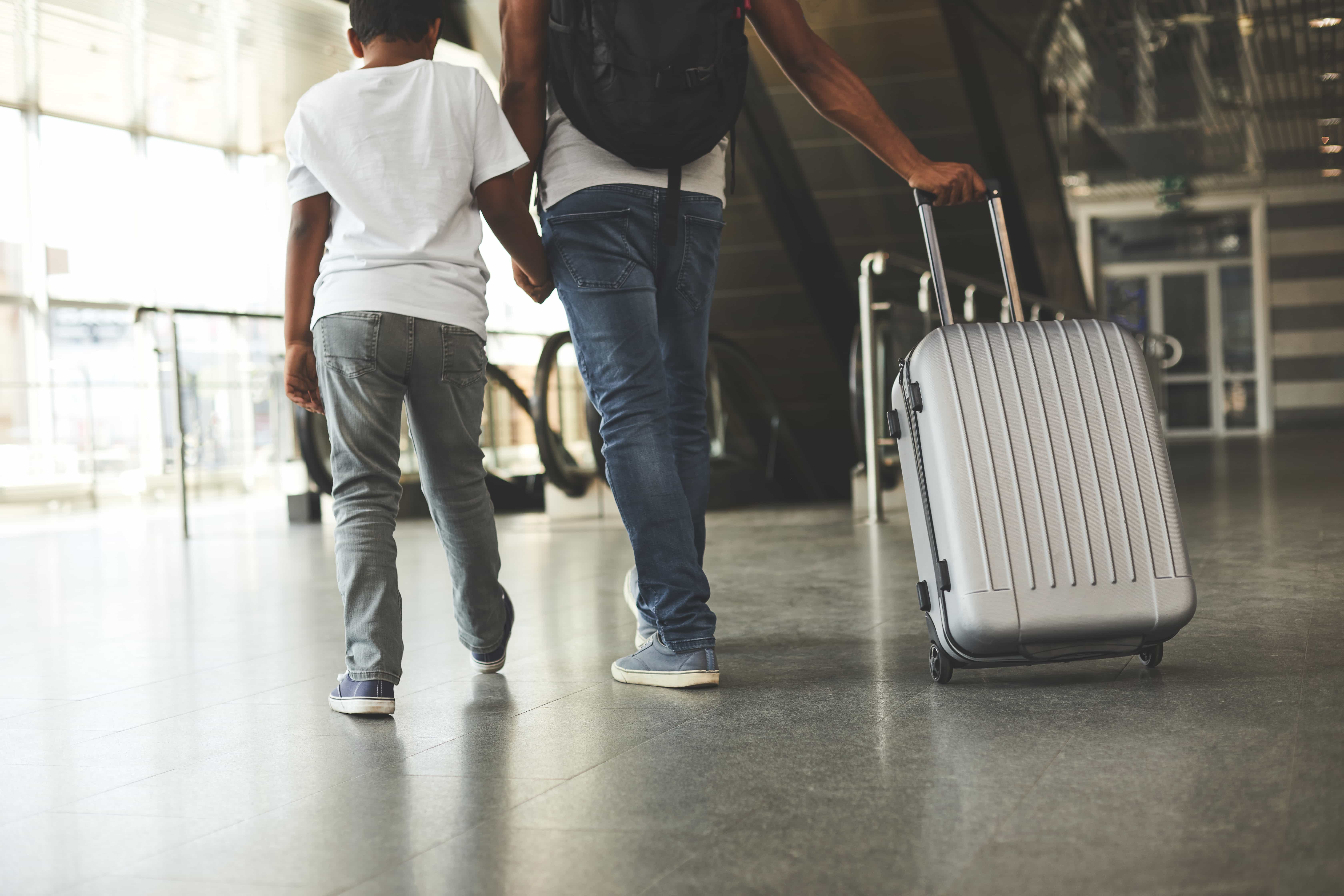 A stock photo of a child holding his father's hand, at the airport.