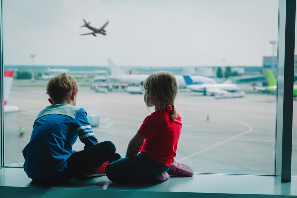 This image accompanies a family law article called "CHILD TAKEN OVERSEAS - WHAT CAN YOU DO?". The image features two children looking at airplanes at the airport.