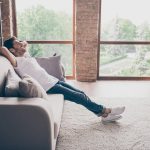 Profile photo of a guy sitting on a cosy sofa holding hands behind his head relaxing and ready to start new life after a divorce