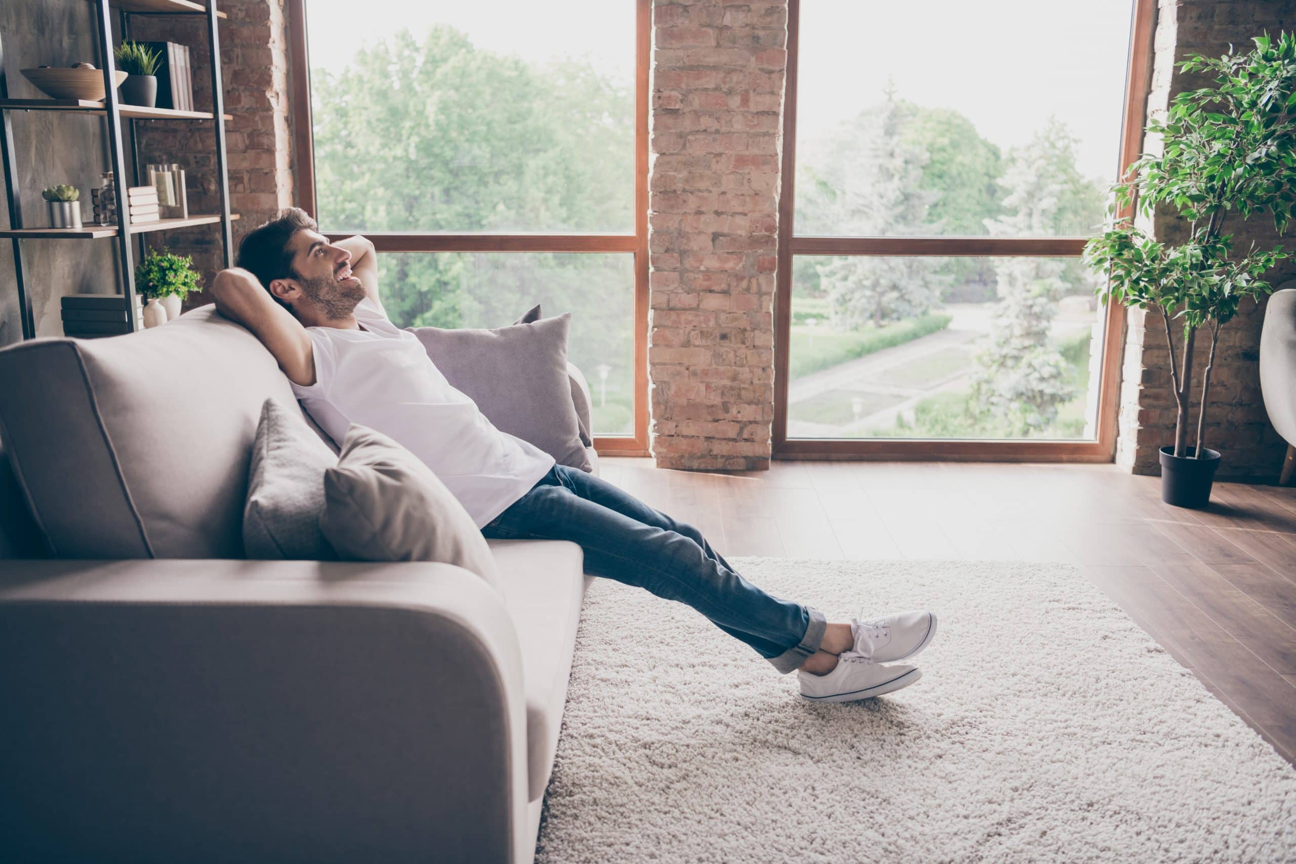 Profile photo of a guy sitting on a cosy sofa holding hands behind his head relaxing and ready to start new life after a divorce