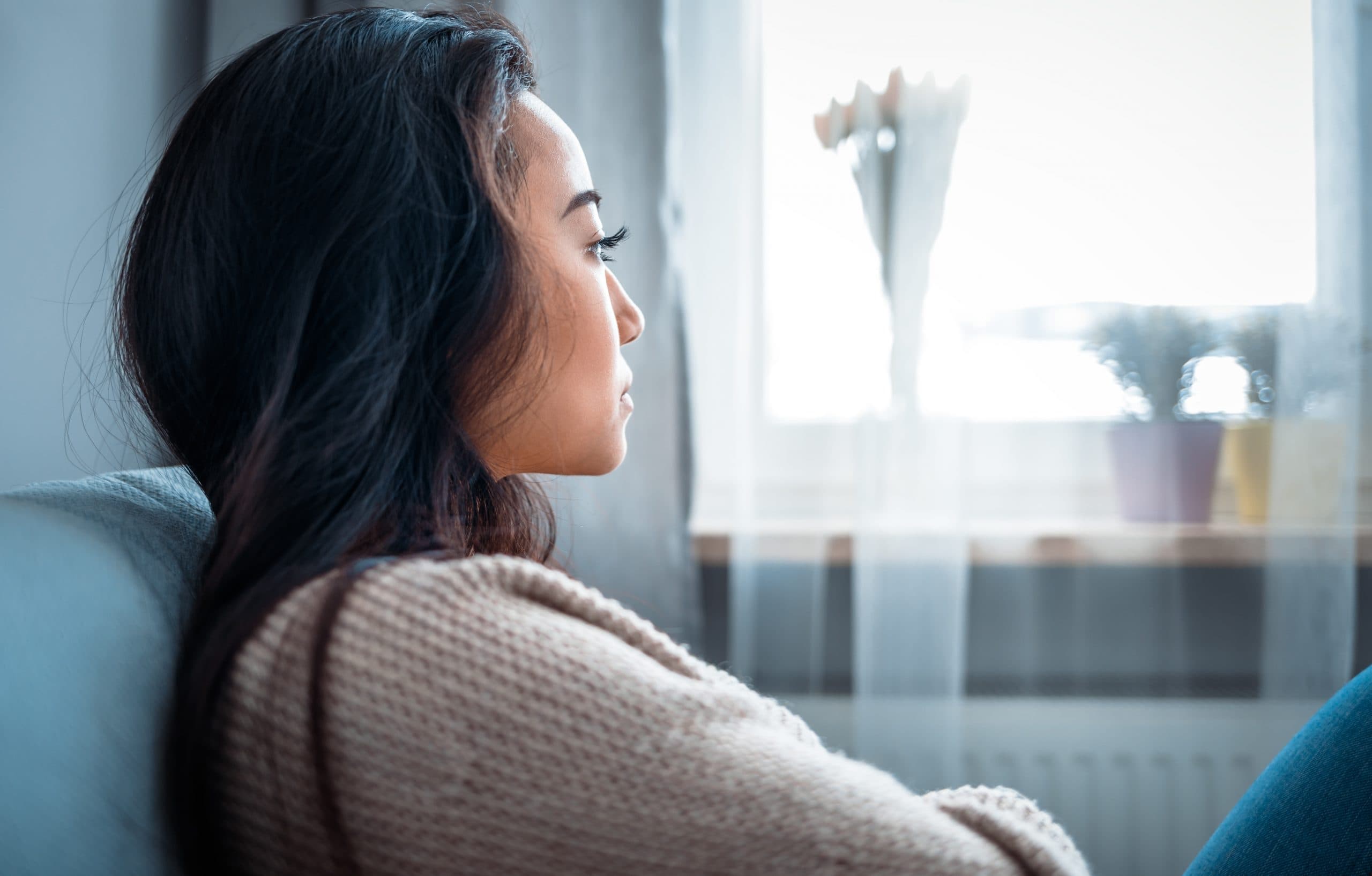 Sad woman sitting on sofa at home and thinking