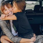 COVID-19 border closures – Can I still see my children? Accompanying picture: Fashionable mother with daughter. Family is sitting in the car trunk. Girl in a black t-shirt is hugging the mother.