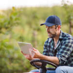 Image of a mature farmer with tablet sitting on mini tractor outdoors accompanying family law article "Rural families in family law settlements"