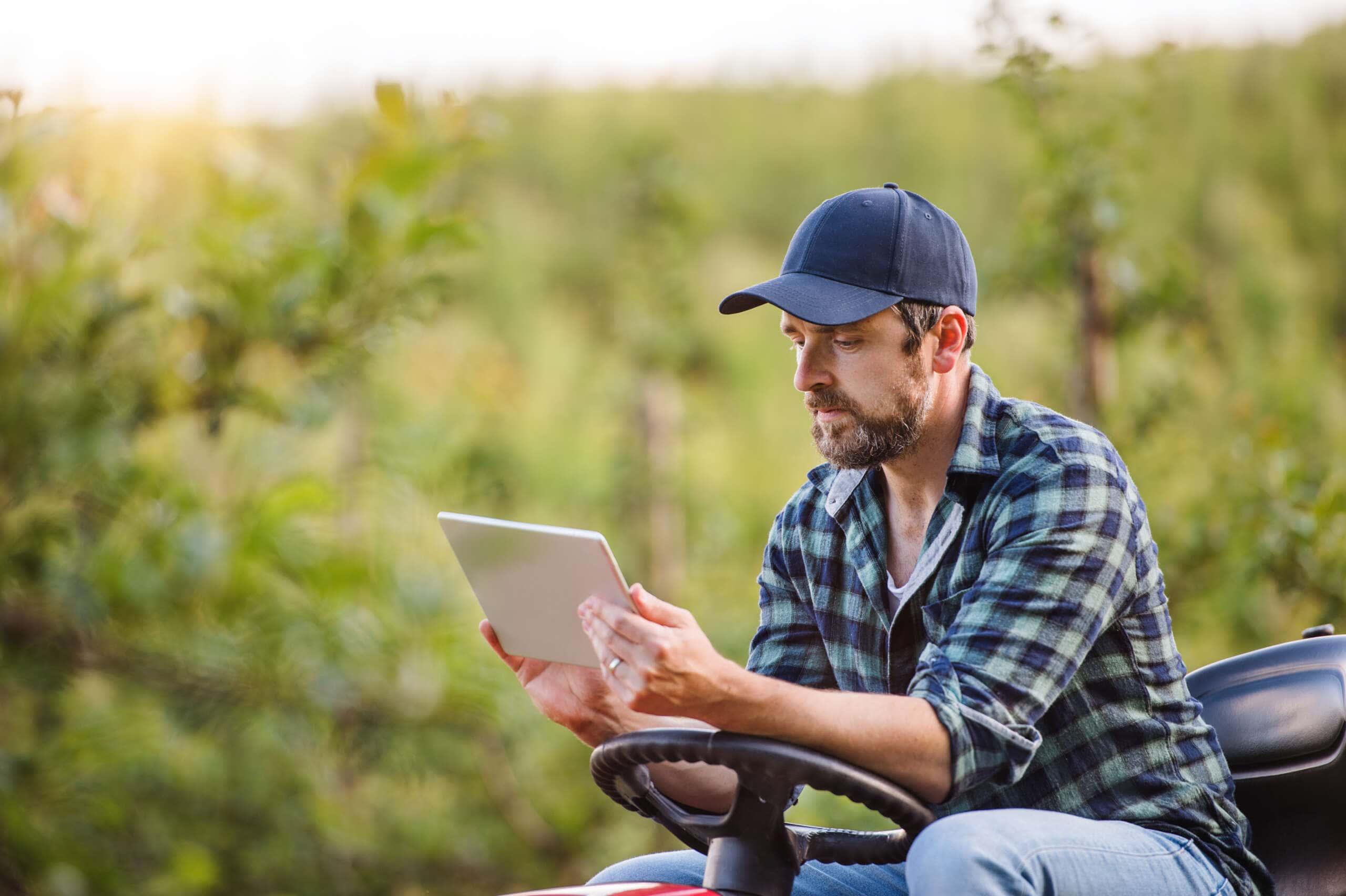 Image of a mature farmer with tablet sitting on mini tractor outdoors accompanying family law article "Rural families in family law settlements"