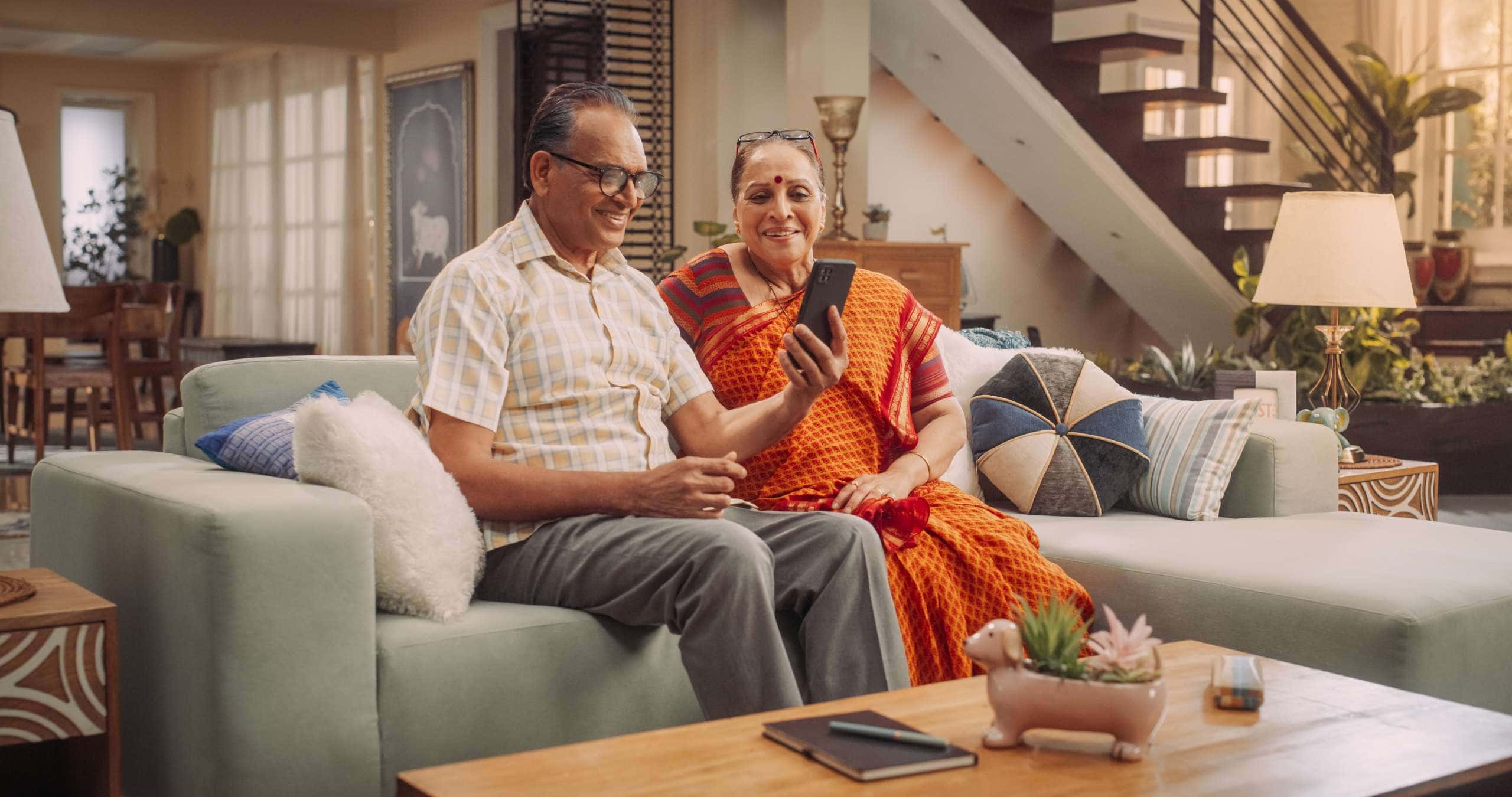 Elderly Couple Using Smartphone for Video Call at Home: Connecting with Loved Ones, Sharing Life’s Moments, and Creating Lasting Memories. Embracing Technology to Stay Close. Medium Shot.